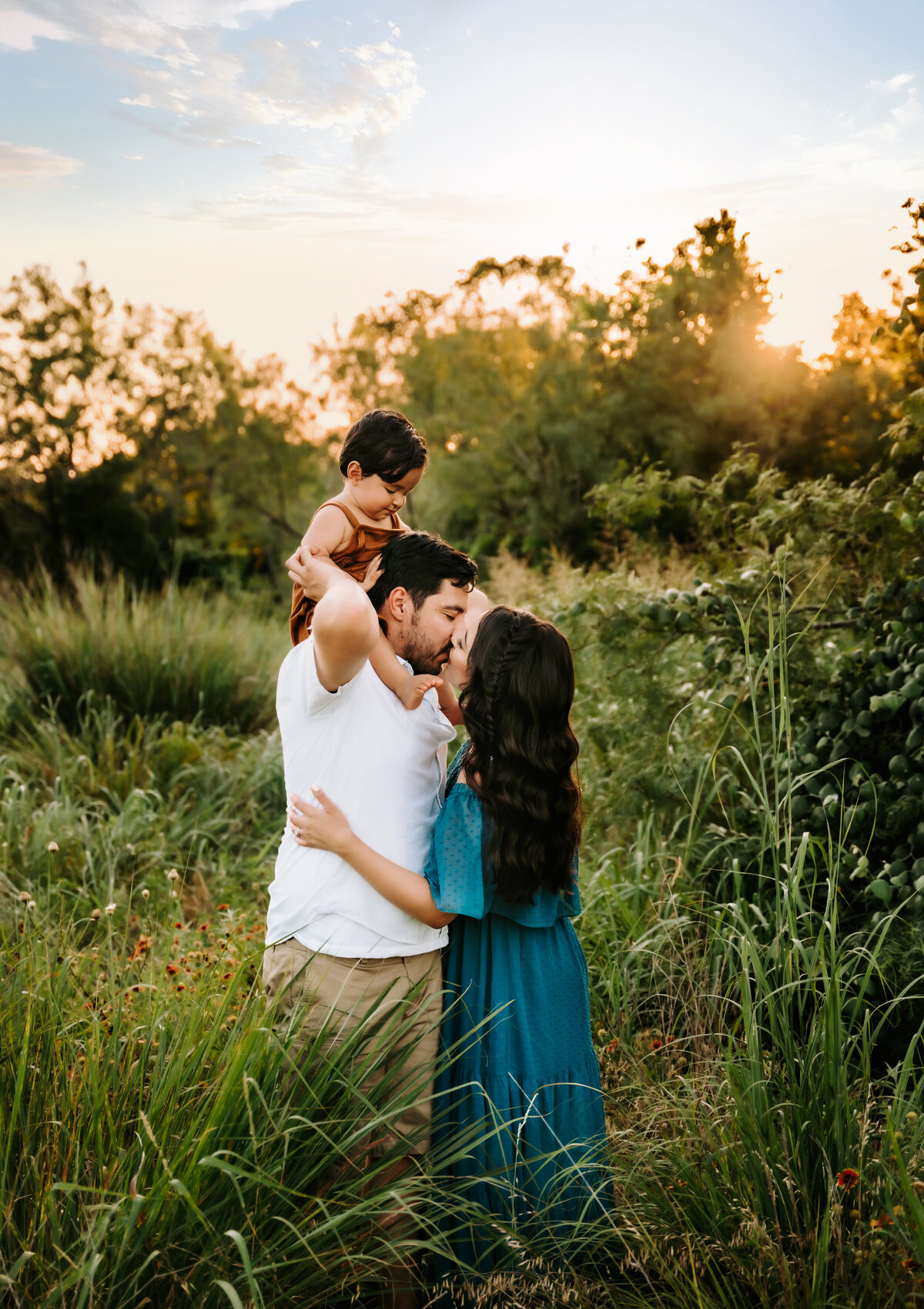 Family Photography, a man kisses his wife, baby on his shoulders