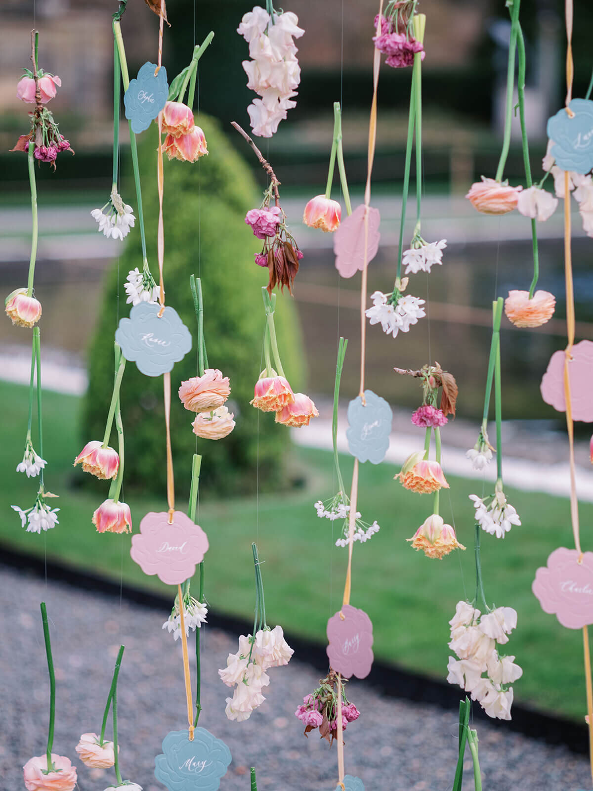paper roses used as escort cards hanging amongst real flowers in the gardens at blenheim palace during a luxury wedding drinks reception