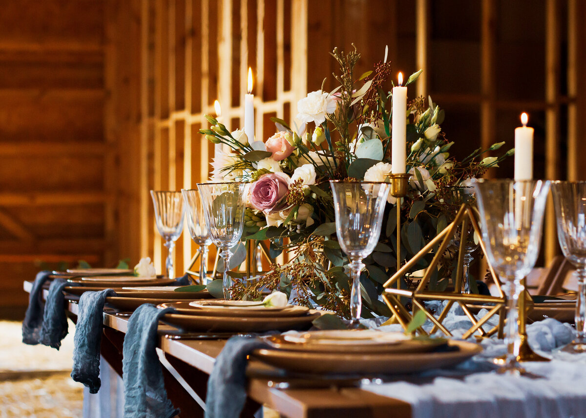 Wedding decor at a dinner table with floral centrepiece and gold glassware, candles and diamond shaped ornaments.