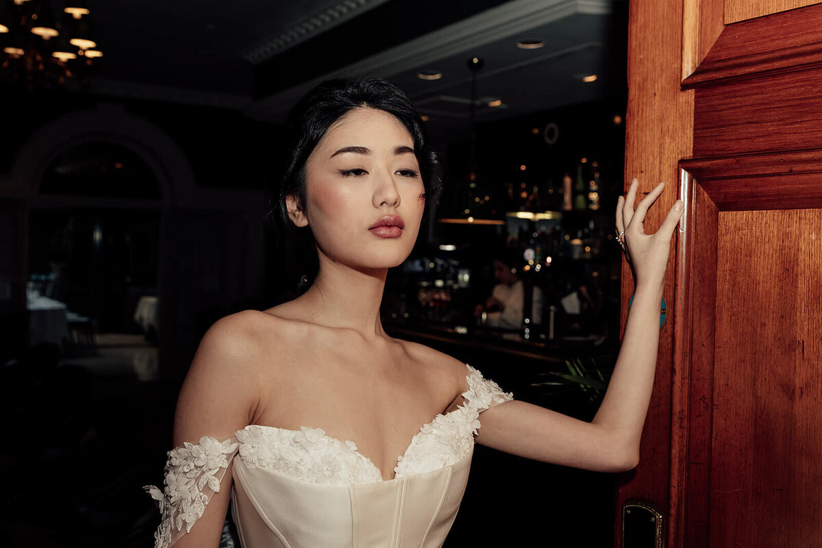 A bride in a Josephine Scott cocktail dress leans on a door in Kensington.