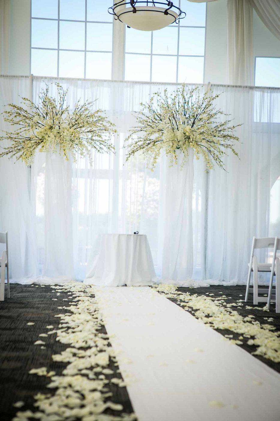 large wedding arch with draped pillars, and large orchid sprays and aisle with petals