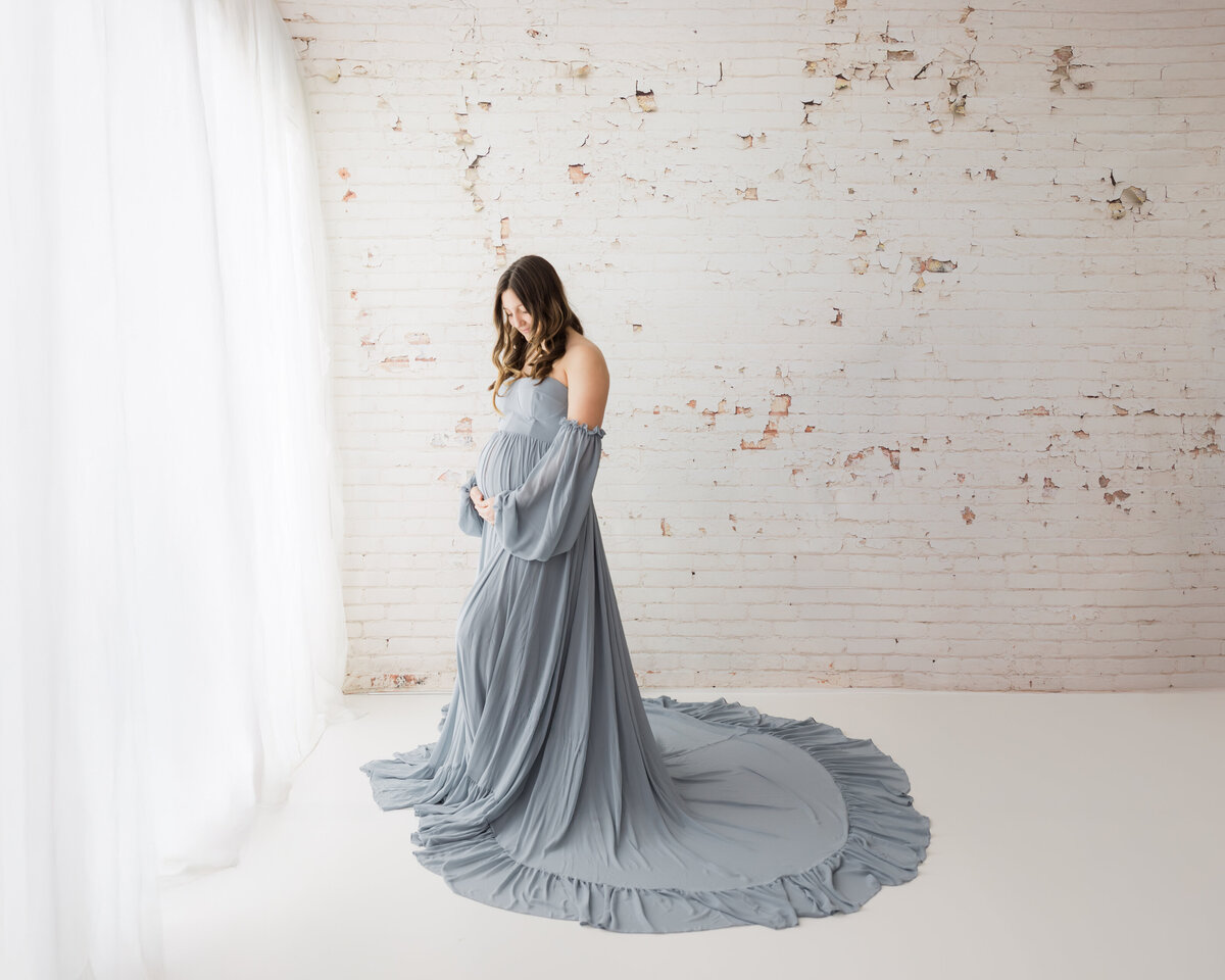 pregnant mother in blue maternity gown holding baby bump for maternity photoshoot