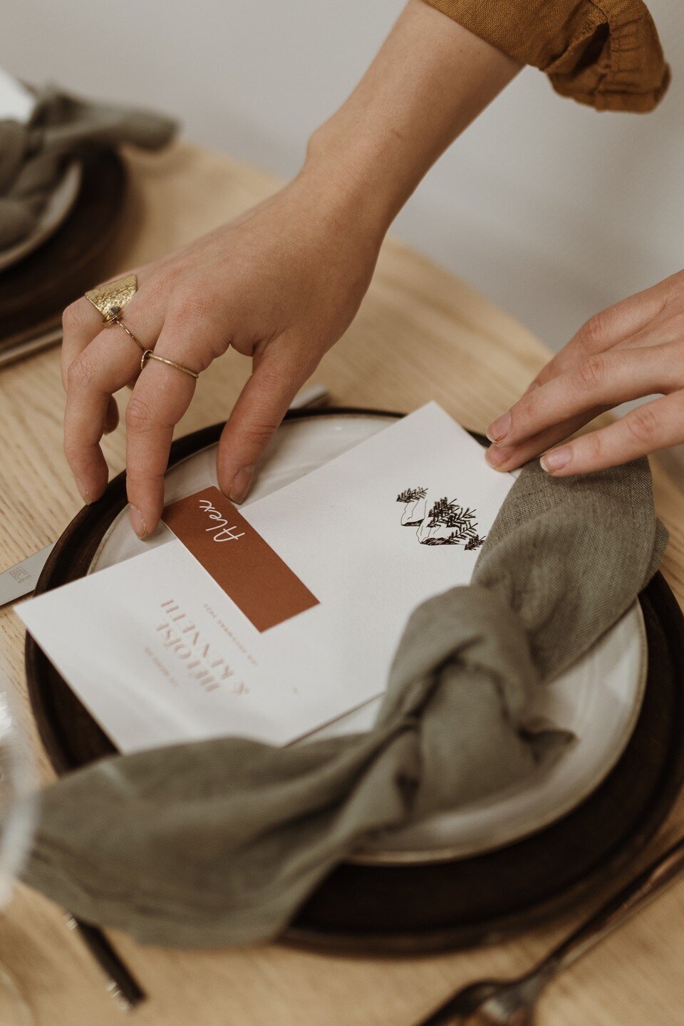 Détail d'une table de mariage, gros plan sur les mains de la fondatrice du repère des pépites qui place les menus dans une assiette