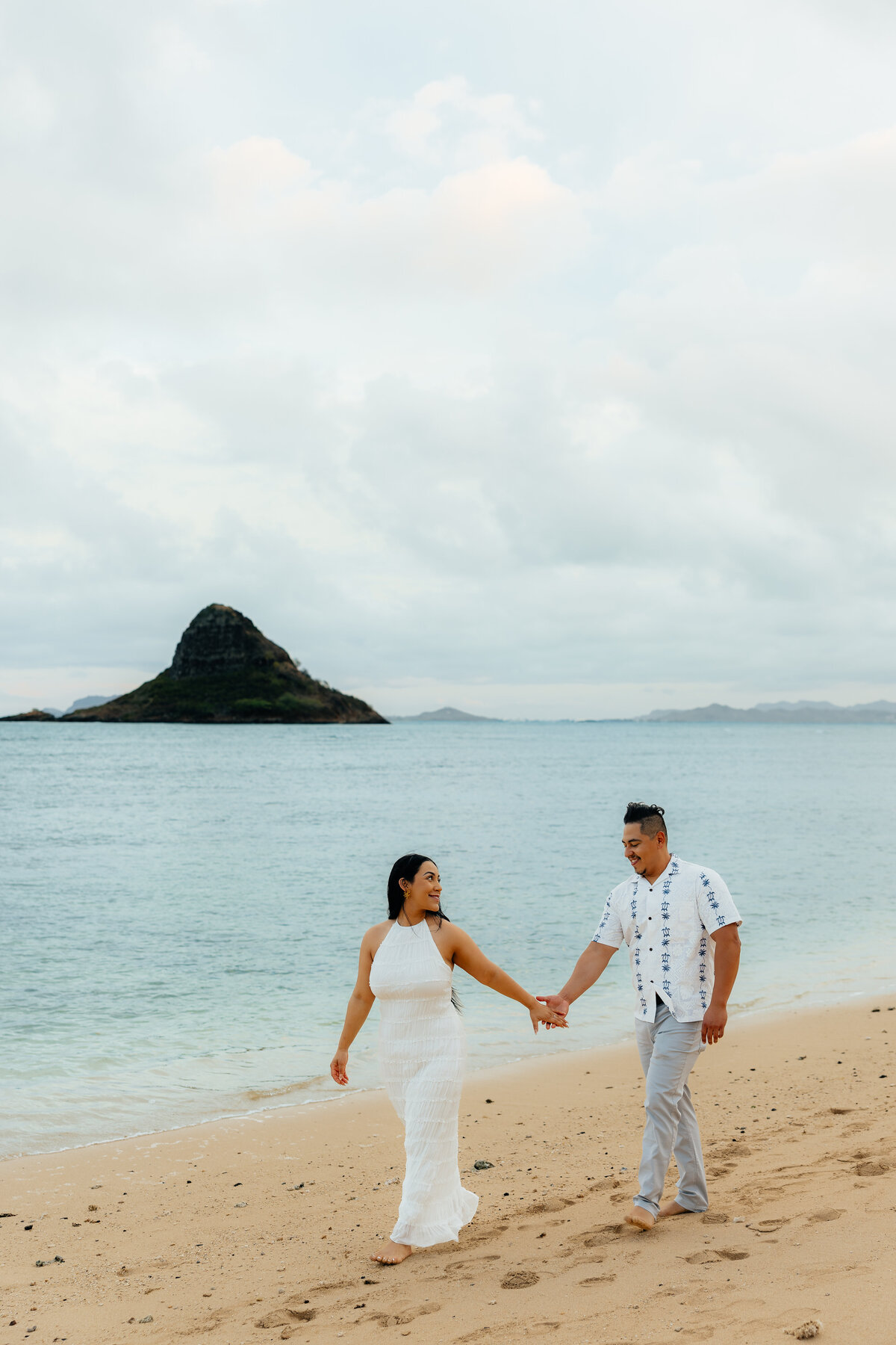Couple holding hands and walking on the beach together at Kualoa Beach at sunset