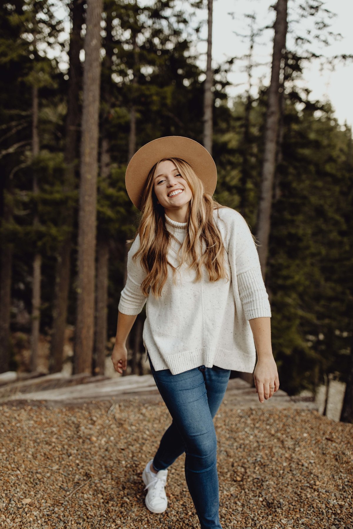 Girl smiling at camera with hat on and in the woods.