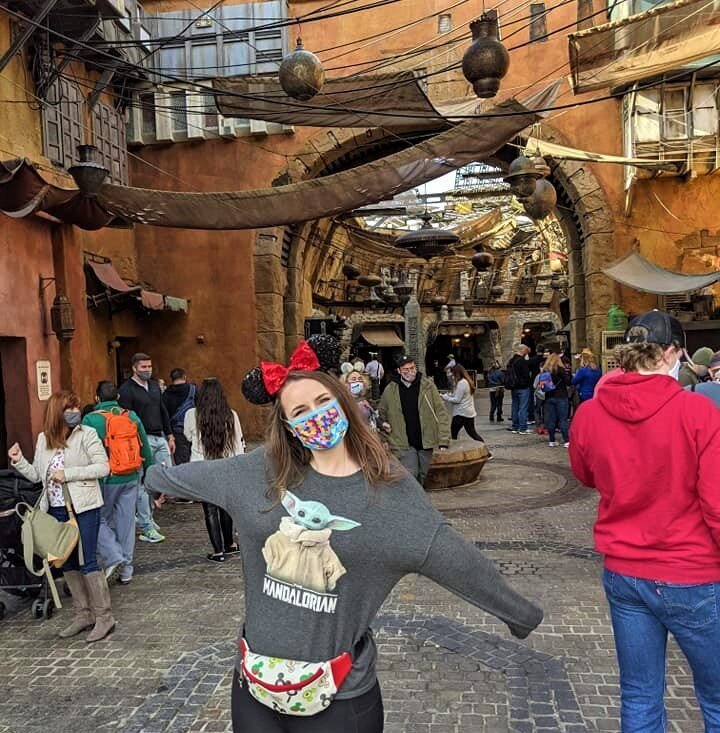 Amy Hord wearing Minnie Mouse ears and a Baby Yoda from The Mandalorian shirt in front of the Black Spire Outpost at Walt Disney World's Galaxy's Edge.