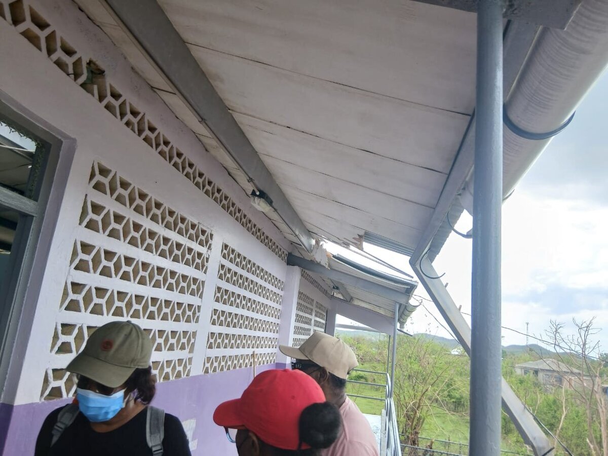 Front walkway covering damaged, with pieces of roofing shifted and community members standing nearby.