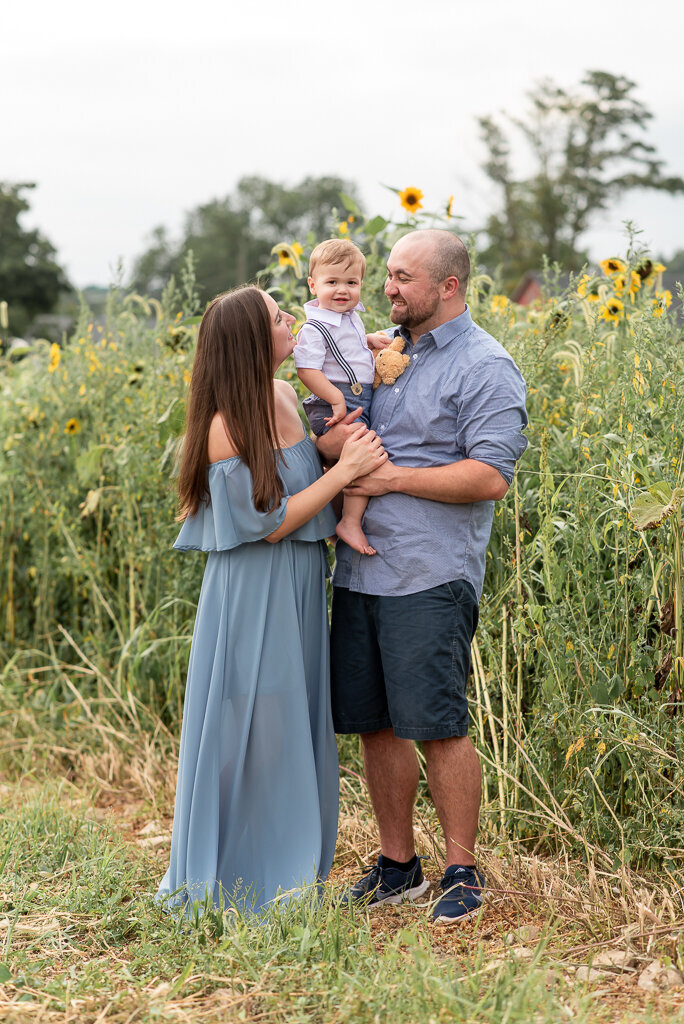 Family of three in sunflower field, dressed in blue