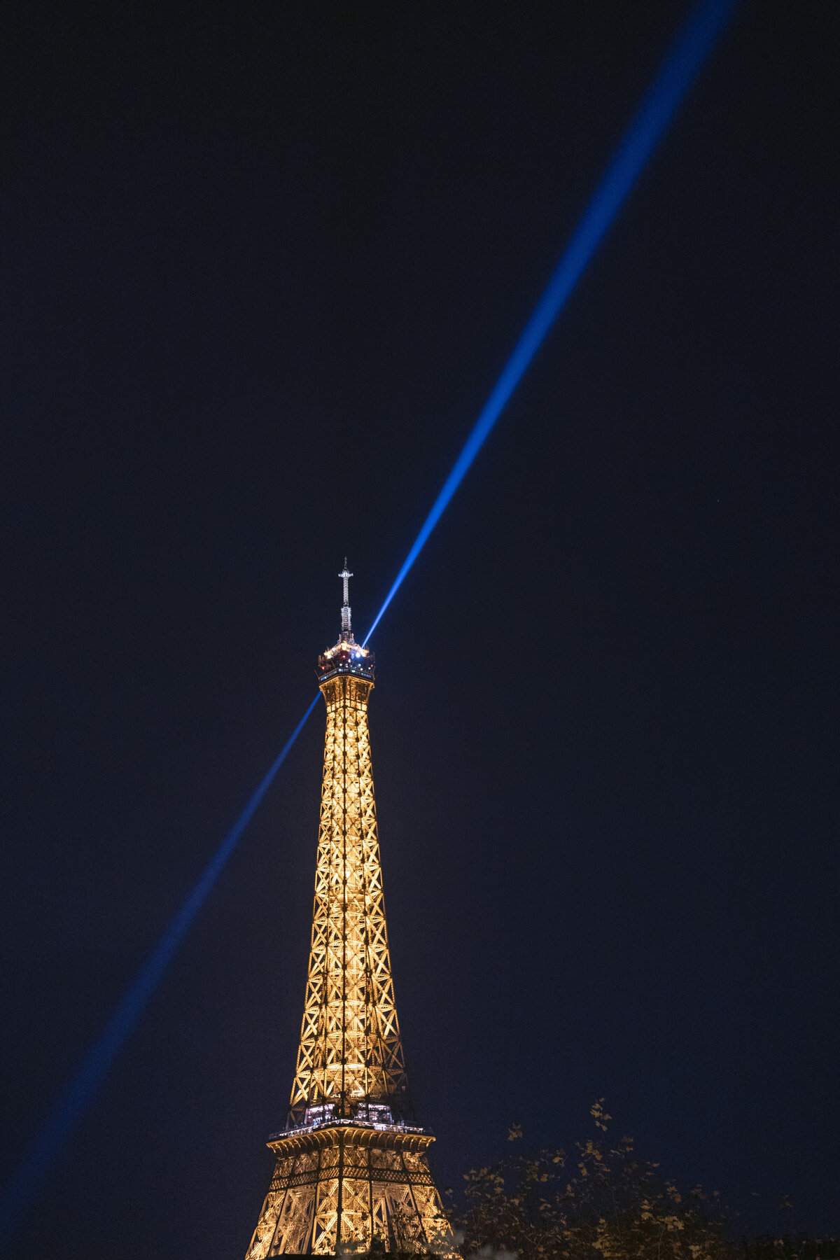 The stunning photo was taken at the iconic Shangri La Hotel & Ritz Paris Hotel in Paris, France, by the talented photographer Matteo Coltro, with videography by Zen Film Works. The nighttime view captures the illuminated Eiffel Tower, with a bright blue beam of light projecting from its pinnacle into the dark sky. The structure exudes a warm glow, beautifully contrasting against the dark backdrop, creating a mesmerizing scene.
