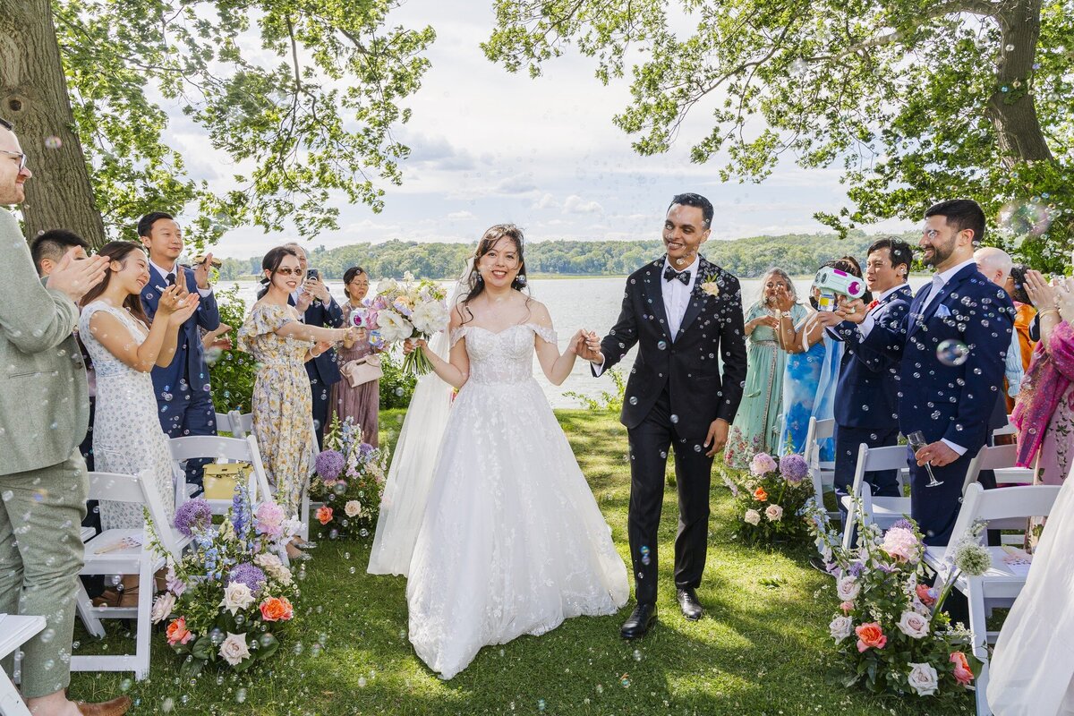 Bride and groom walking down the aisle at a lakeside Hudson Valley wedding ceremony as guests cheer