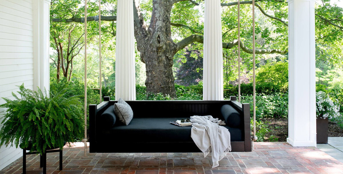 Historic home design in New England featuring original brick pavers, classic Greek columns, and a modern black daybed on a covered porch.
