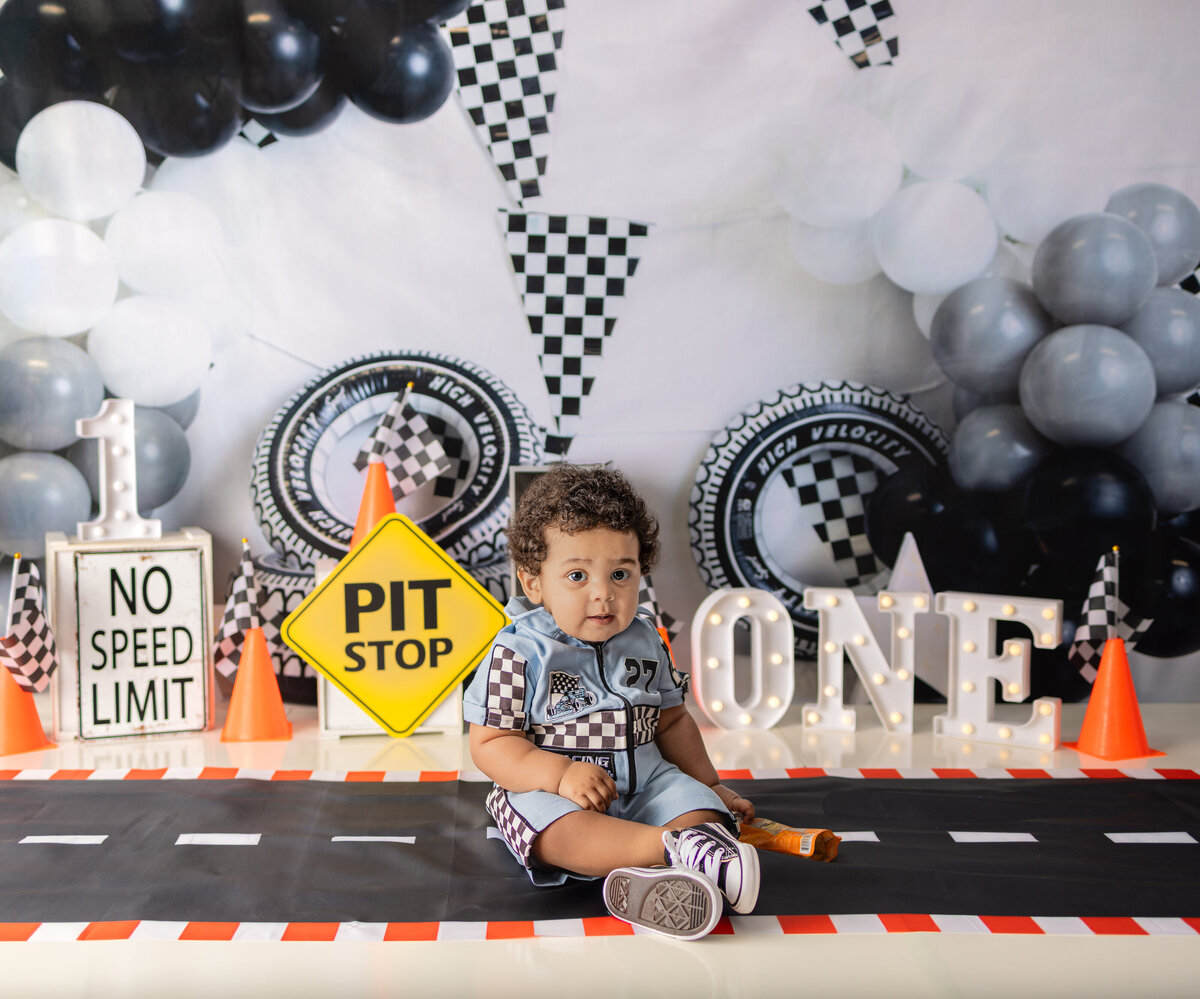 Baby boy in race car outfit sitting on road backdrop for race-themed first birthday cake smash session in Waldwick NJ studio