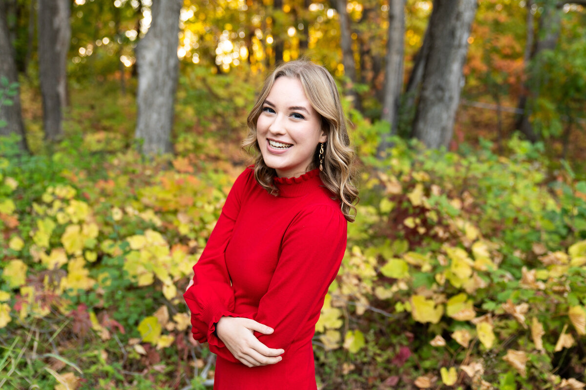 Girl wearing a red dress poses in the woods for her senior pictures