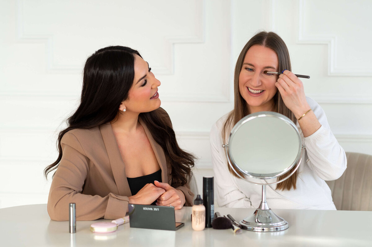 a student smiling while she applies her eyeshadow during in-person makeup lesson with Stephanie Bullock Makeup Artistry.  Captured by Ottawa Branding Photographer JEMMAN Photography COMMERCIAL