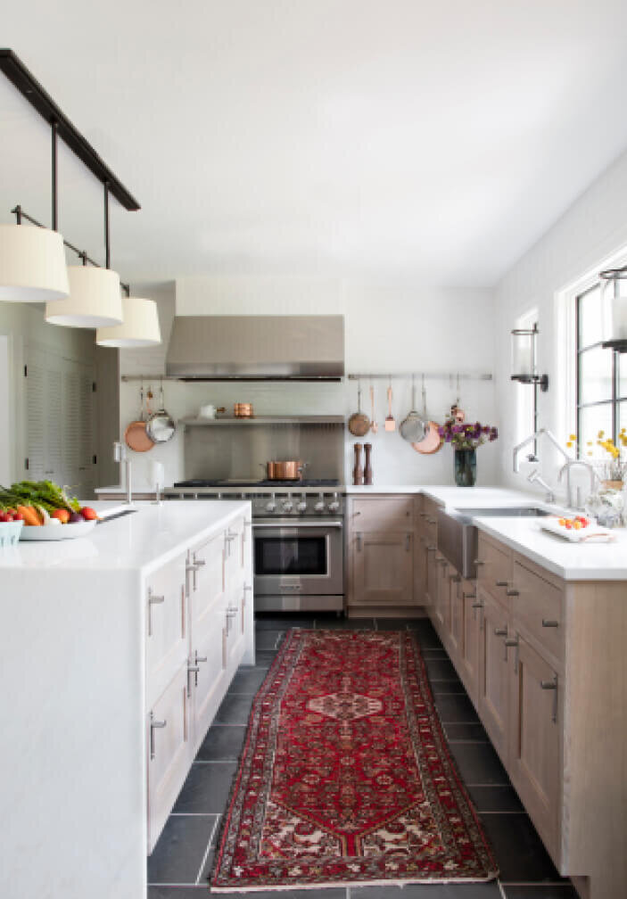 Kitchen designers in Westwood design a natural wood kitchen with white counters, a stainless steel range and hood, bronze lighting, slate flooring, and a vintage runner.