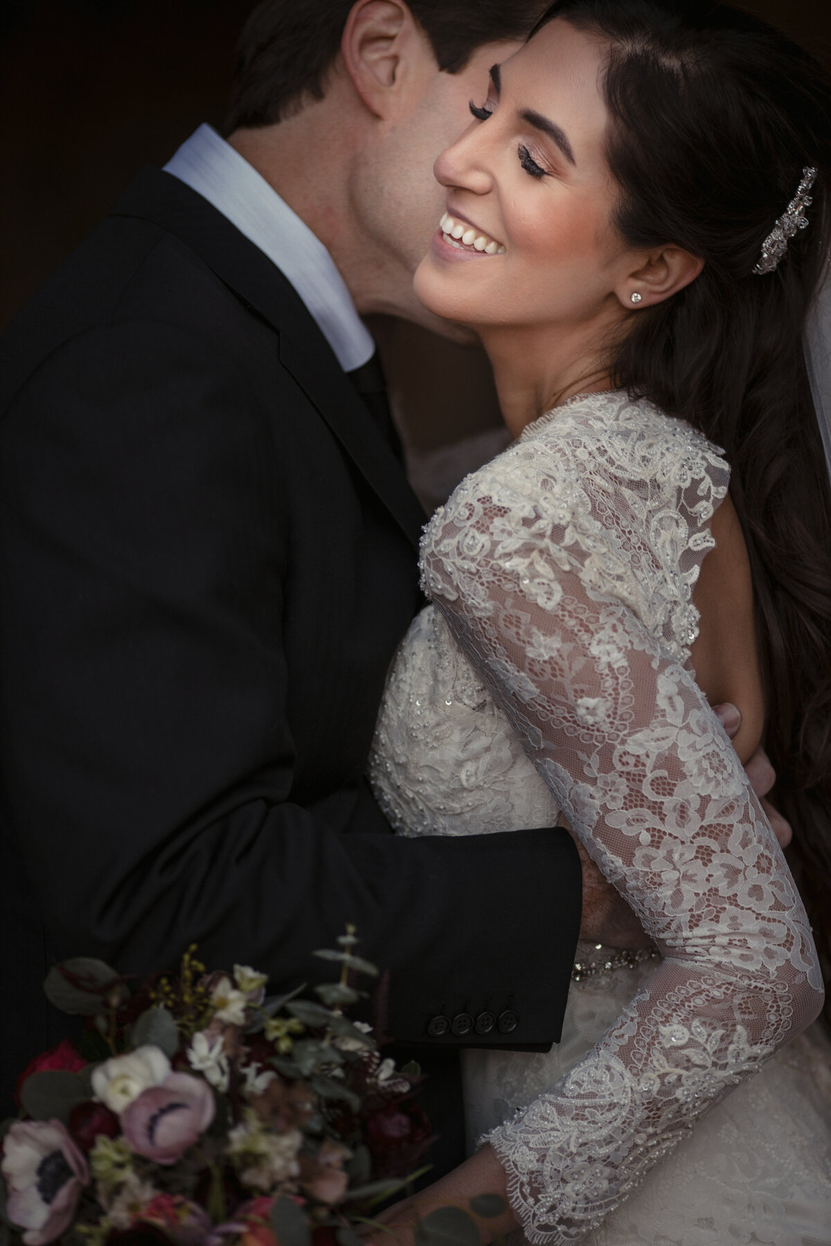 A groom kissing a bride's cheek as she smiles.