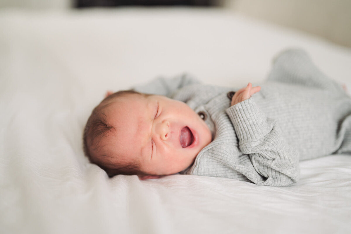 baby yawning while laying on a bed