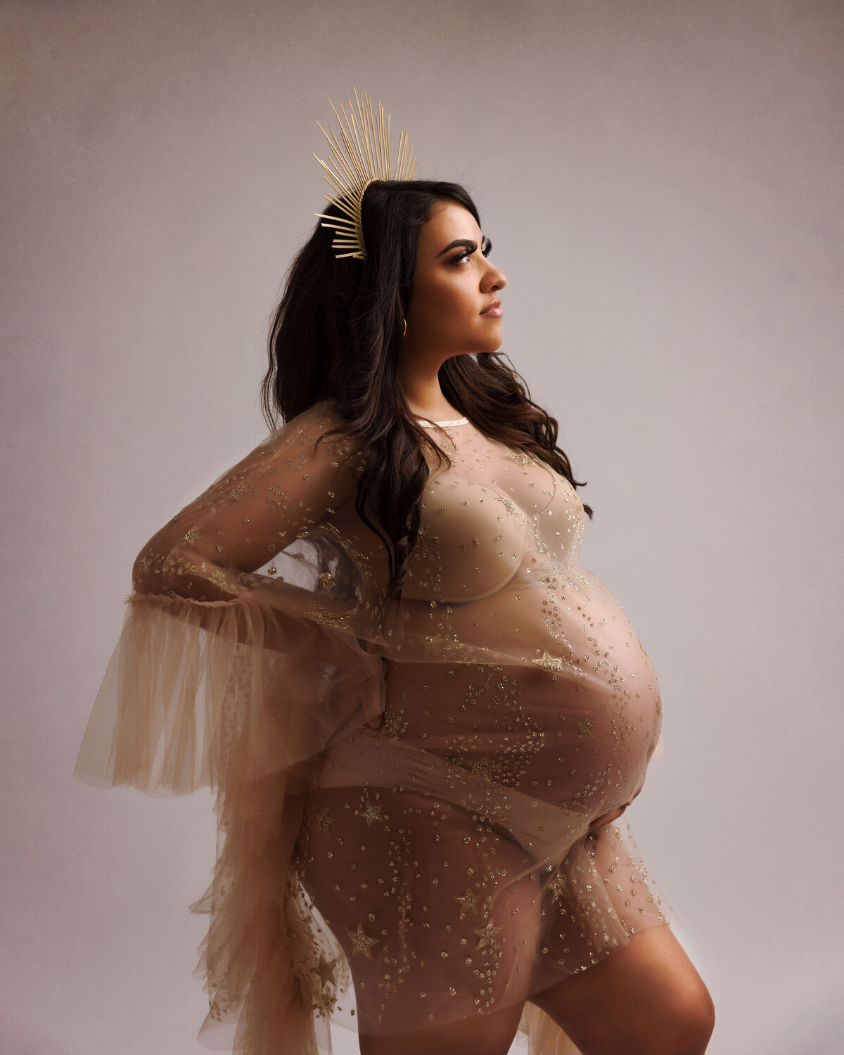 maternity photo session in studio wearing a see through tan boudoir gown in tan and a majestic crown  near dupont