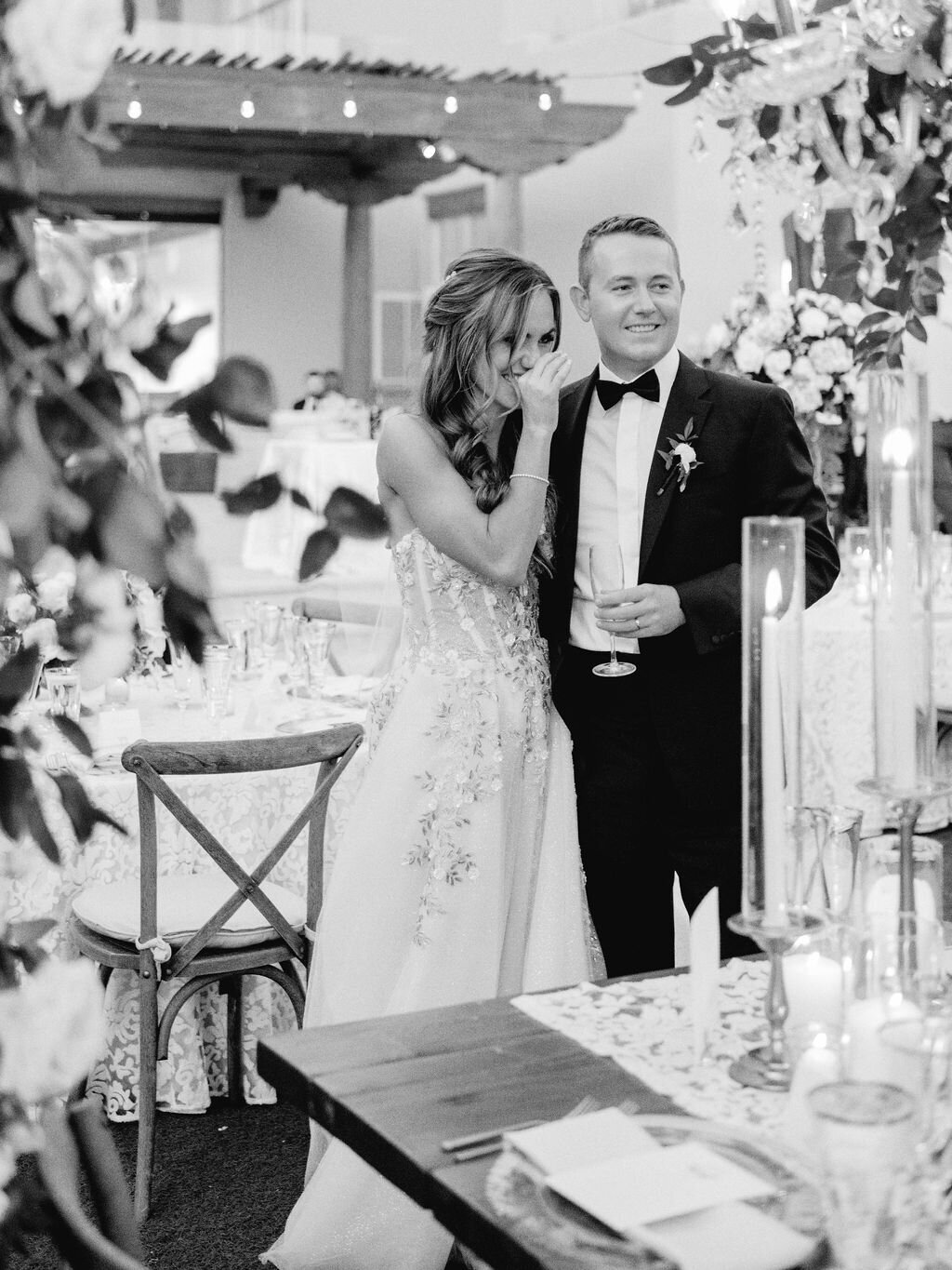 A joyful bride and groom share a heartfelt moment at their wedding reception, surrounded by elegant candlelit decor and floral arrangements.