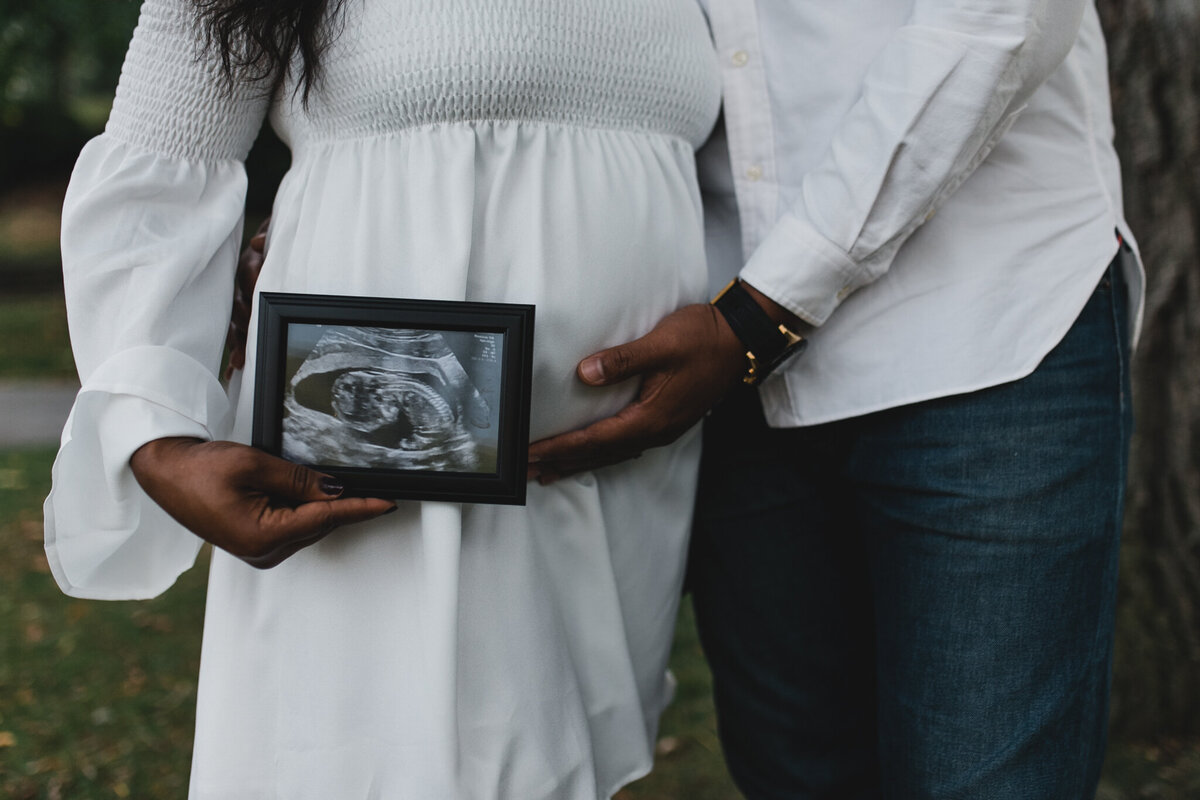 Maternity shot with soon to be mom, and dad kissing holding ultra sound photo.