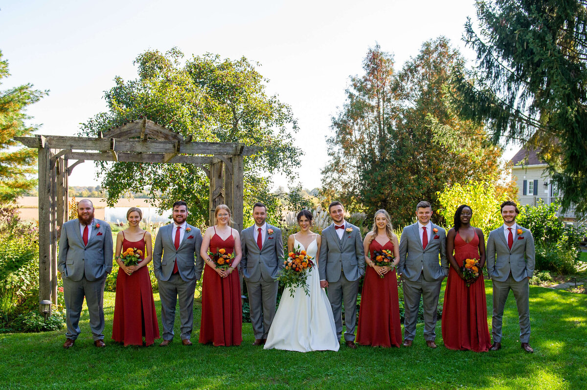 a group photo of an Ottawa wedding bridal party at Strathmere venue.  The bridesmaids are wearing long burgundy dresses; the groomsmen are wearing grey suits.  Captured by Ottawa wedding photographer JEMMAN Photography