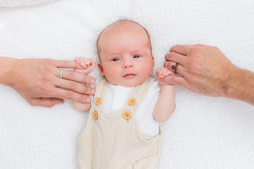 Parents hold a newborn's hands.