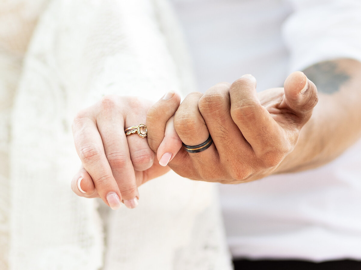 Close-up of hands interlocked by the pinkies and showing wedding rings to camera