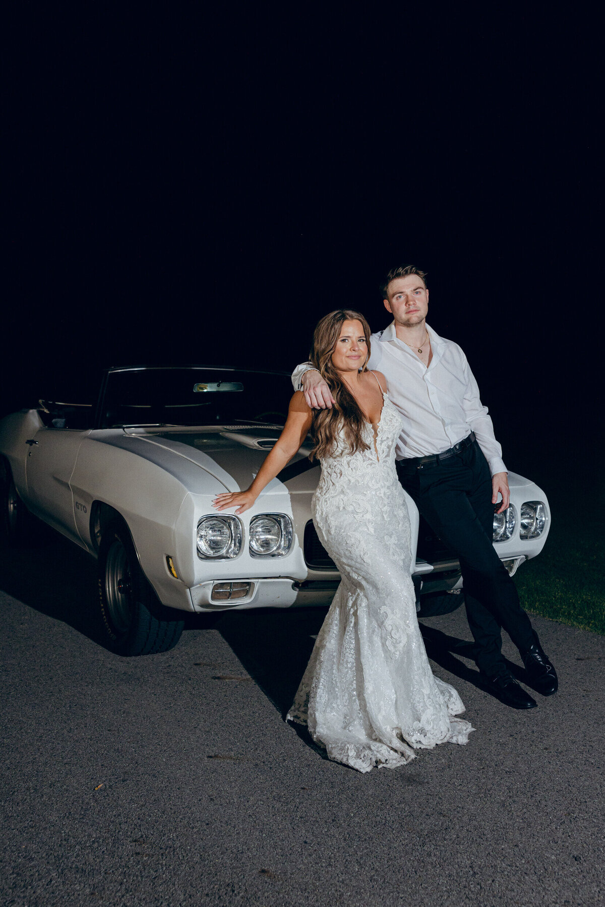 A wedding photo of the bride and groom posing with their getaway car at the end of the wedding reception