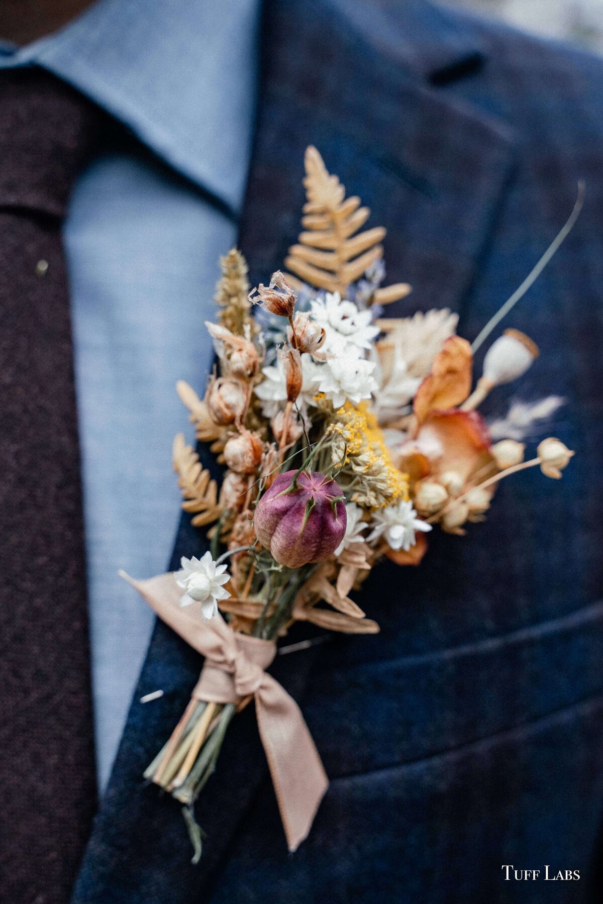 Boutonniere with dried flowers pinned on dark blue suit for an outdoor winter wedding.