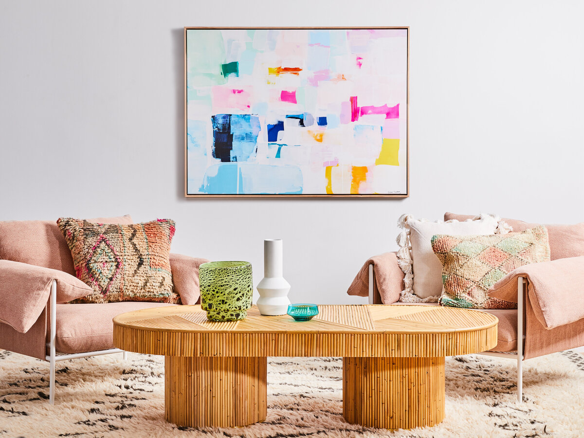 Residential interior design project by interior stylist in Melbourne, showcasing a modern living room with abstract artwork, pink armchair, colorful cushions, and natural wood coffee table. Interior decorator service for Sandringham residential space. 