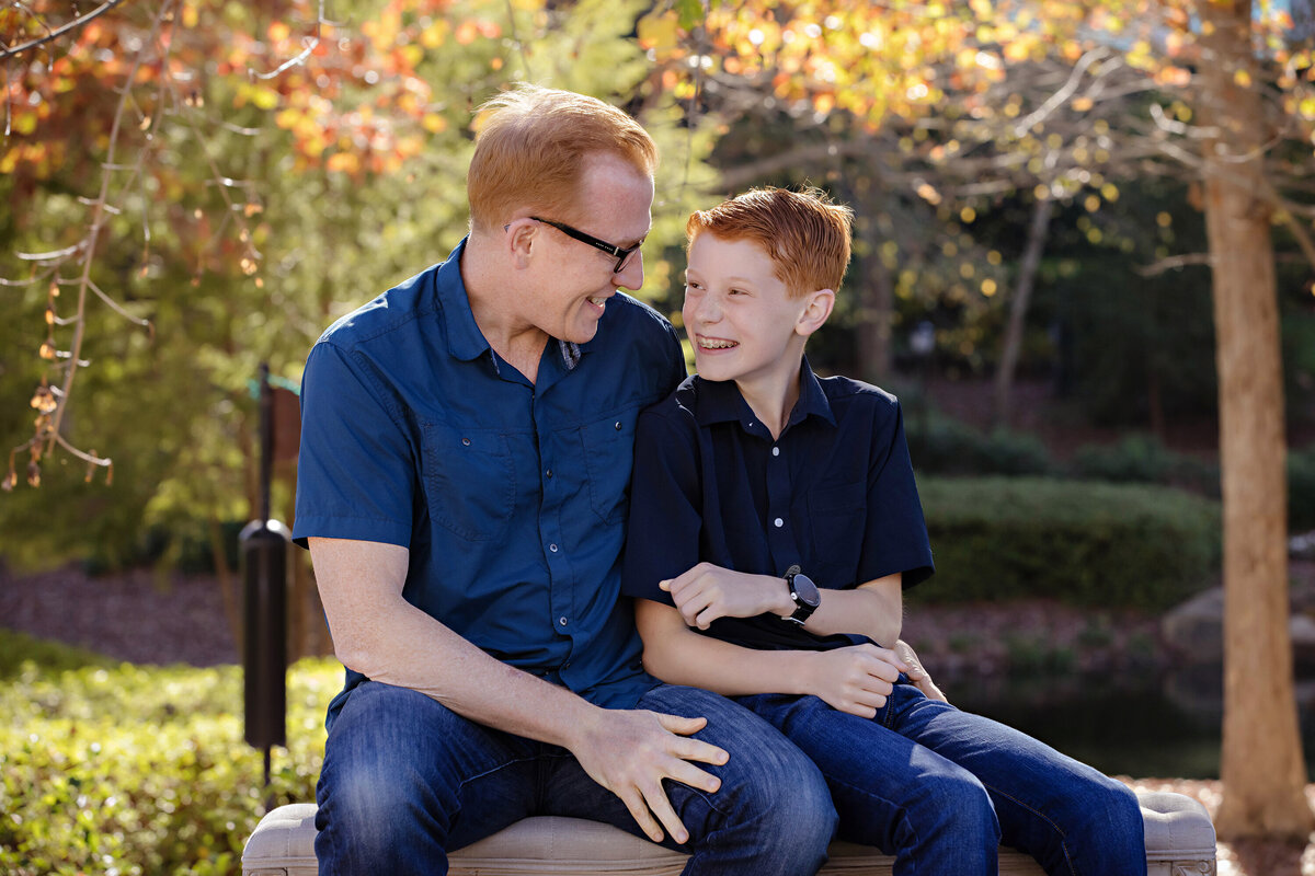 Candid autumn portrait of dad and son on a park bench surrounded by brilliant foliage at Ballantyne Corporate Park