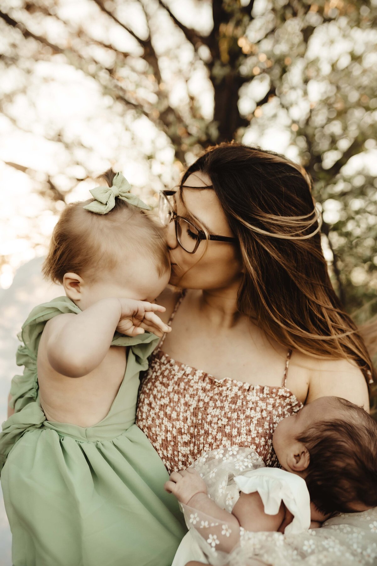 Mother holding toddler and newborn baby during golden hour in a Missouri field