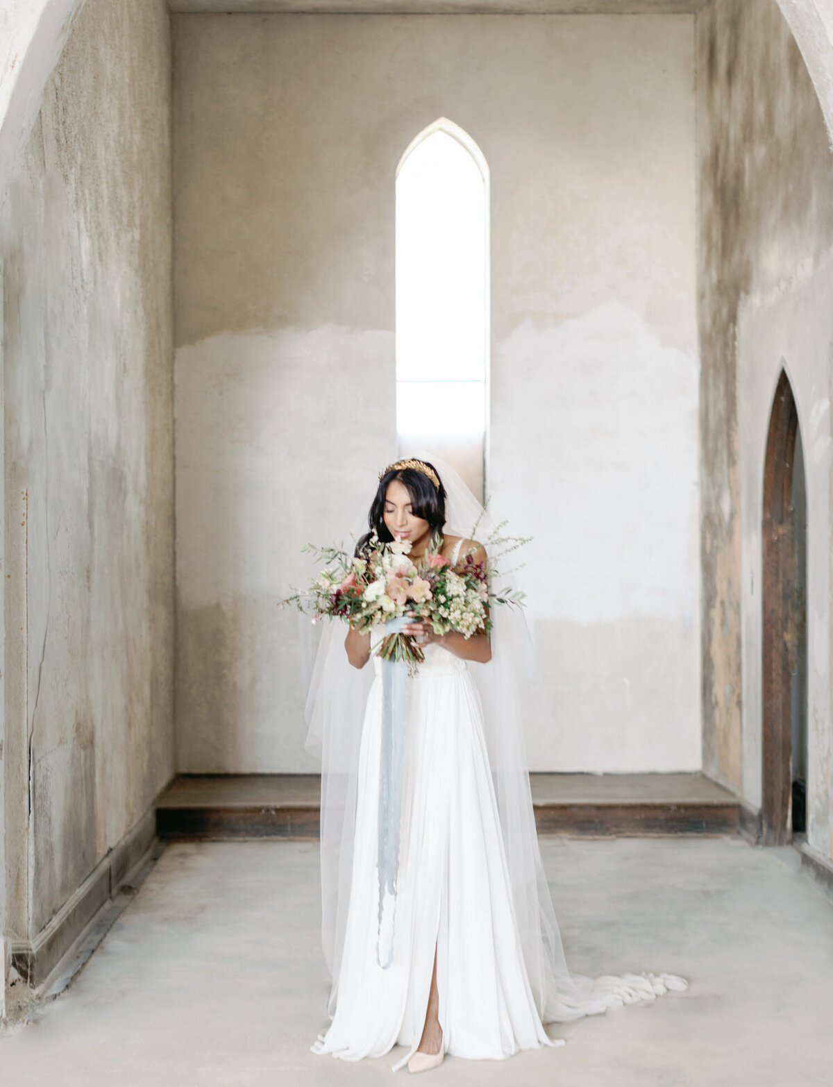 indian bride smells colorful bouquet under crumbling arches, abandoned cathedral wedding in Italy