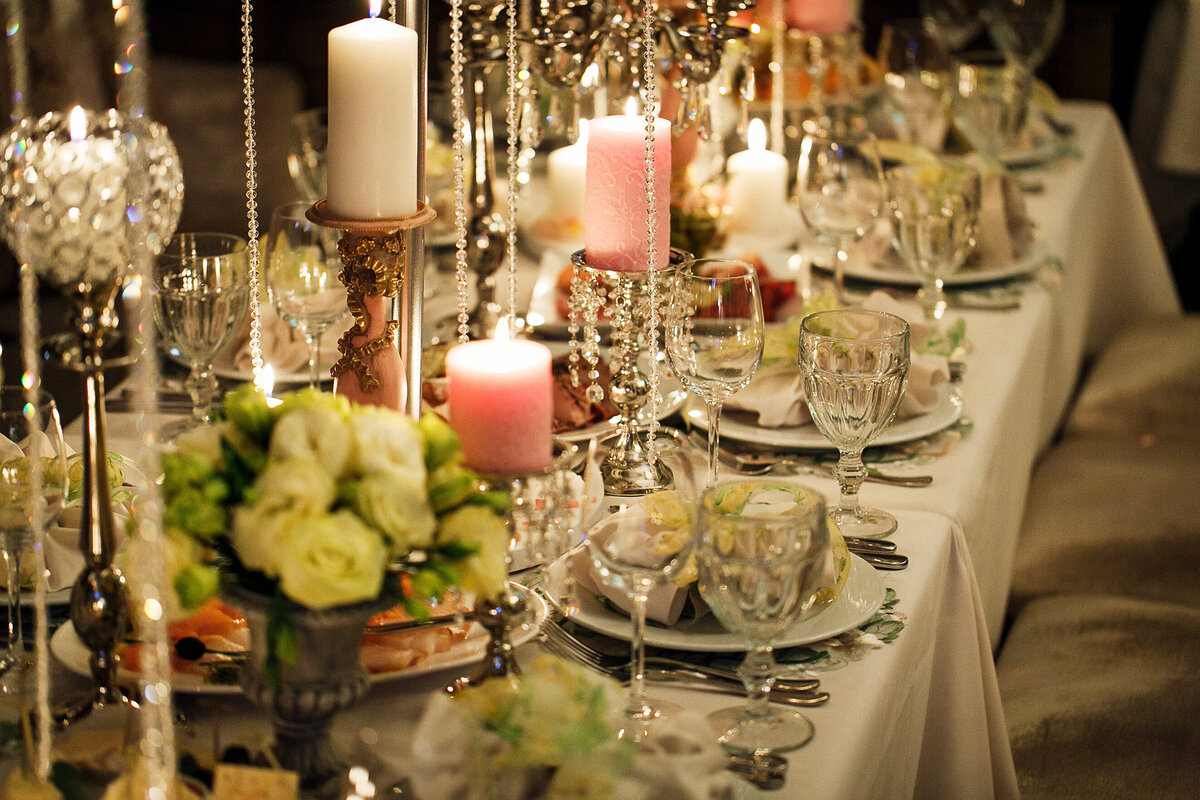 An opulent wedding tablescape featuring glowing candles, cascading hanging beads, and intricate floral centerpieces. The refined details and elegant ambiance create a romantic and sophisticated reception setting, perfect for couples seeking a high-end wedding aesthetic.