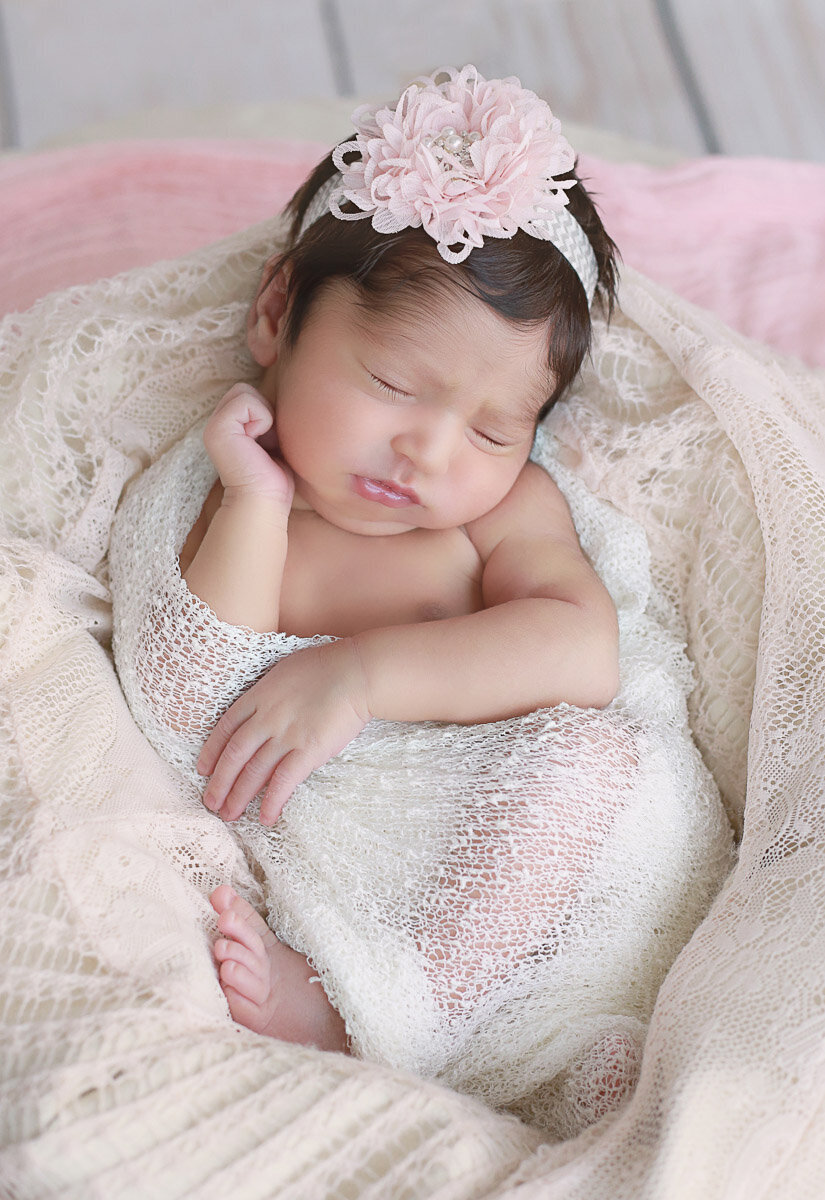 Newborn baby girl wearing flower hairband sleeping during her home newborn photo session in Calgary Alberta