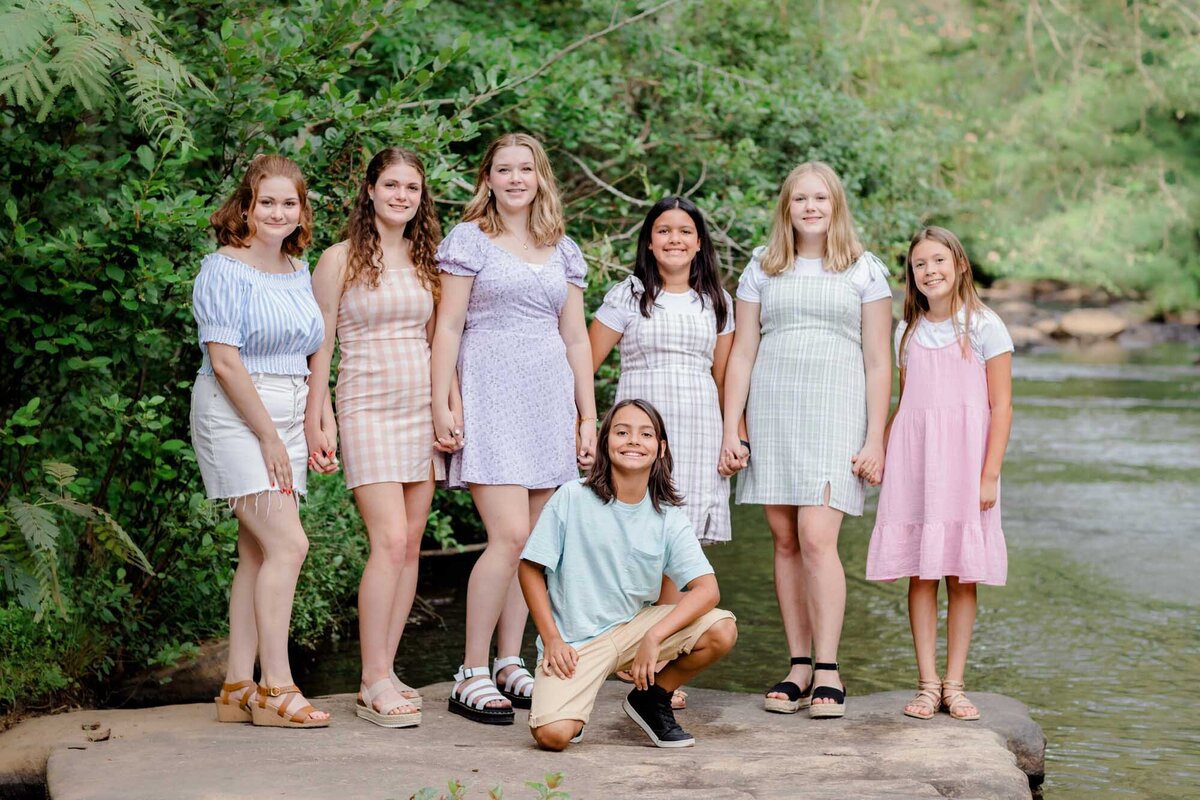 An extended family session with three families of cousins on a rock with a creek behind them.