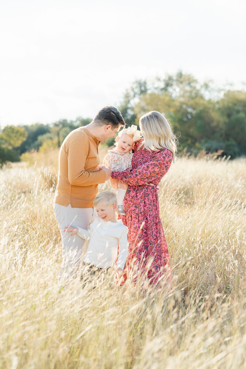 a father tickles his young daughter while she is held by her mother in this candid photo captured by a family photographer in Austin, TX.