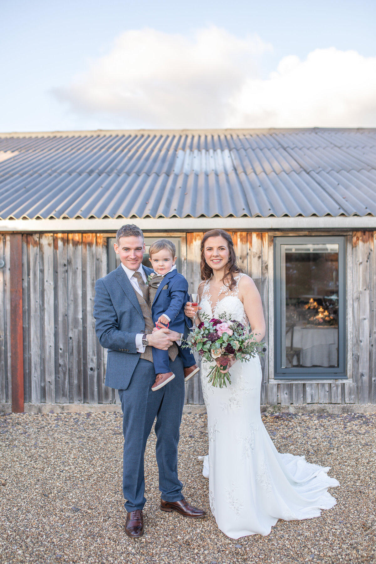 Bride and groom group photo with son standing outside wedding barn