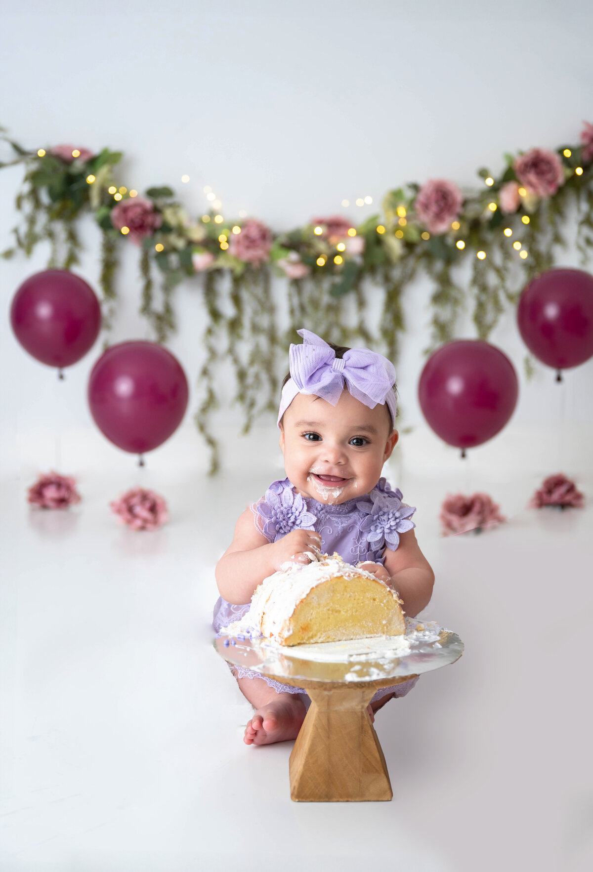 Smiling baby sitting while holding half of a cake which is flipped over. 