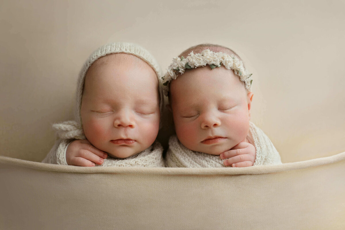 newborn twin babies laying side by side on a tan abric at their newborn photo session