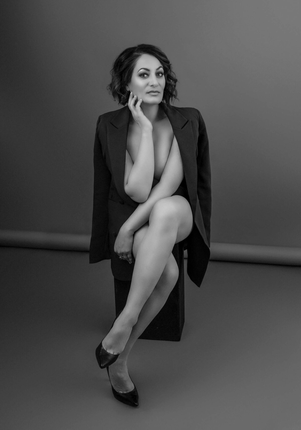 Black and white portrait of a confident woman in a blazer, sitting with crossed legs, exuding strength and elegance.