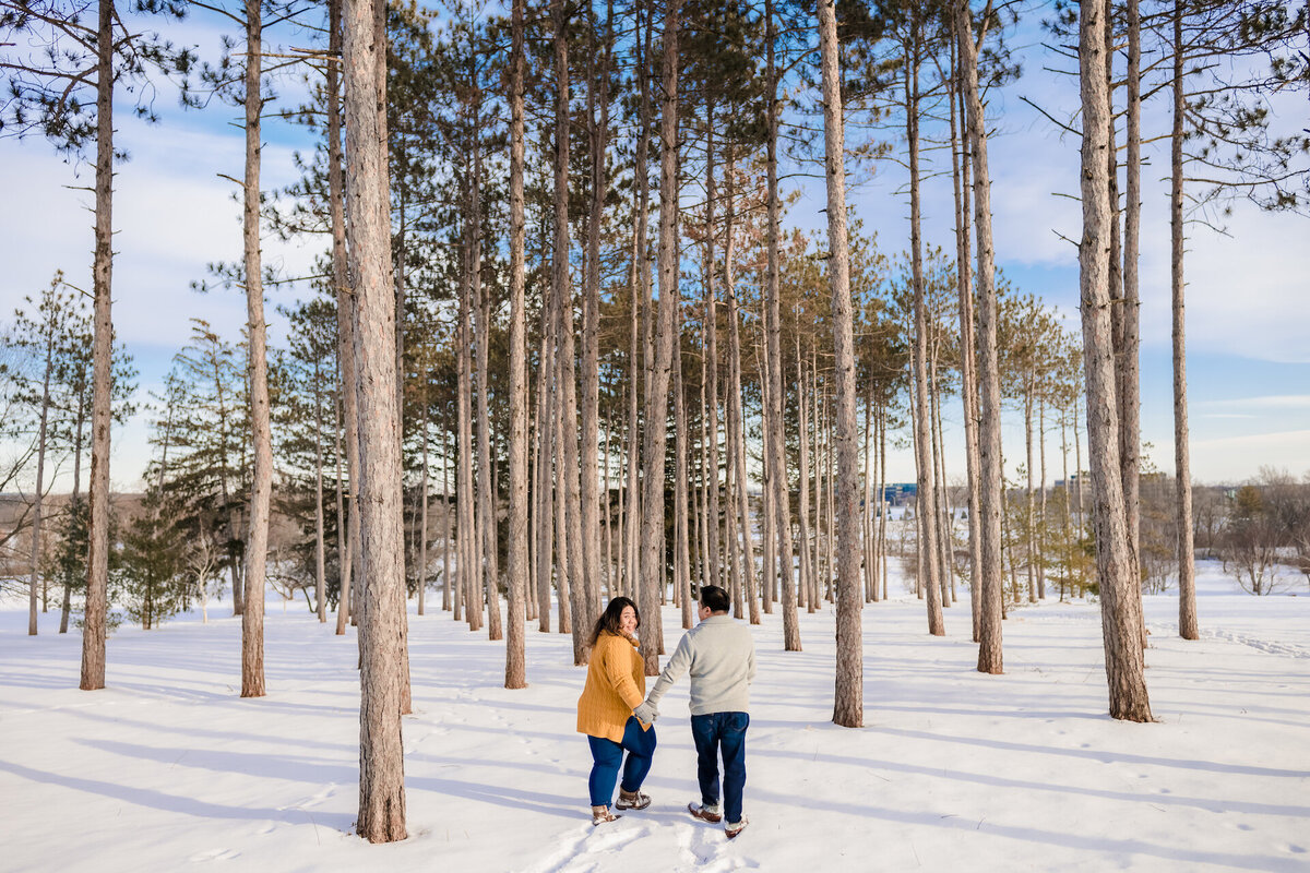 A couple runs through snow in a pine trees  forest in winter.