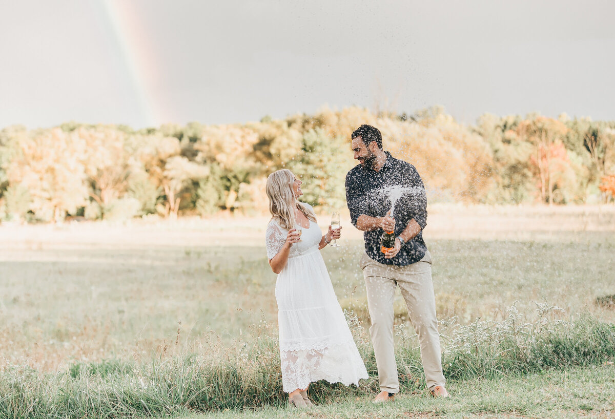 Couple popping champaign under a rainbow at their summer engagement session in London Ontario