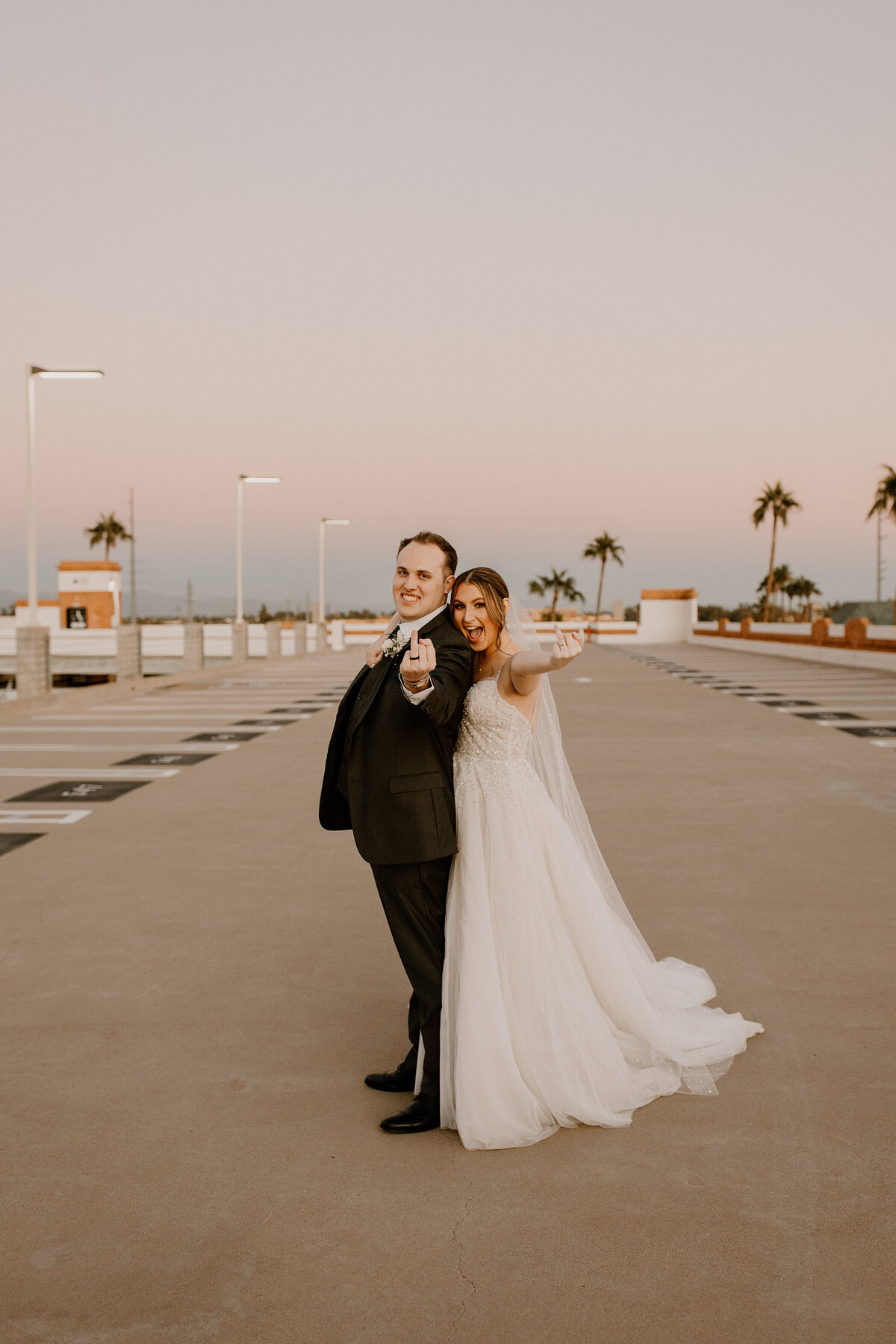 A married couple standing in a parking lot holding out their ring fingers.