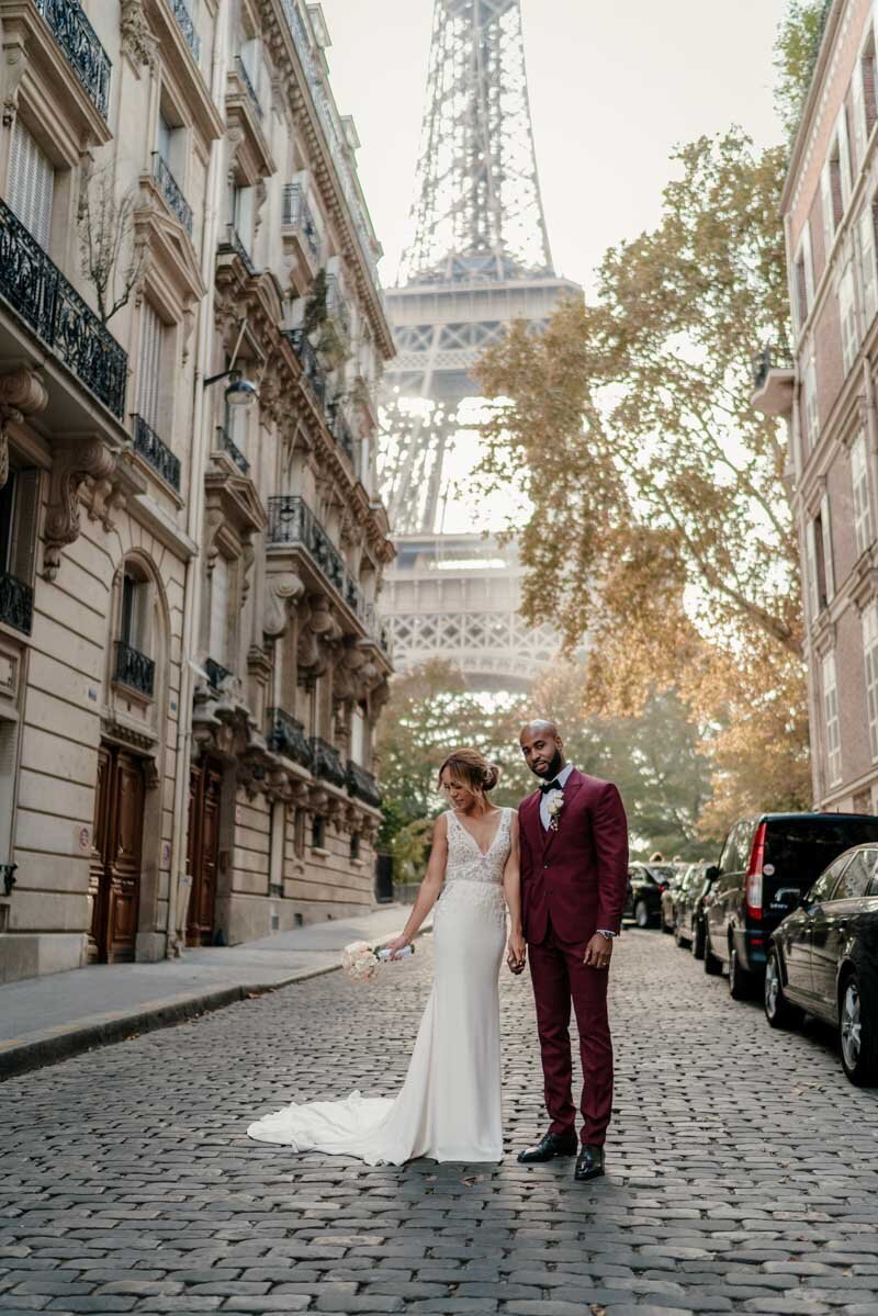 Un couple métisse pose dans une rue pavée de Paris avec la Tour Eiffel en arrière-plan, lors de leur séance photo de mariage.