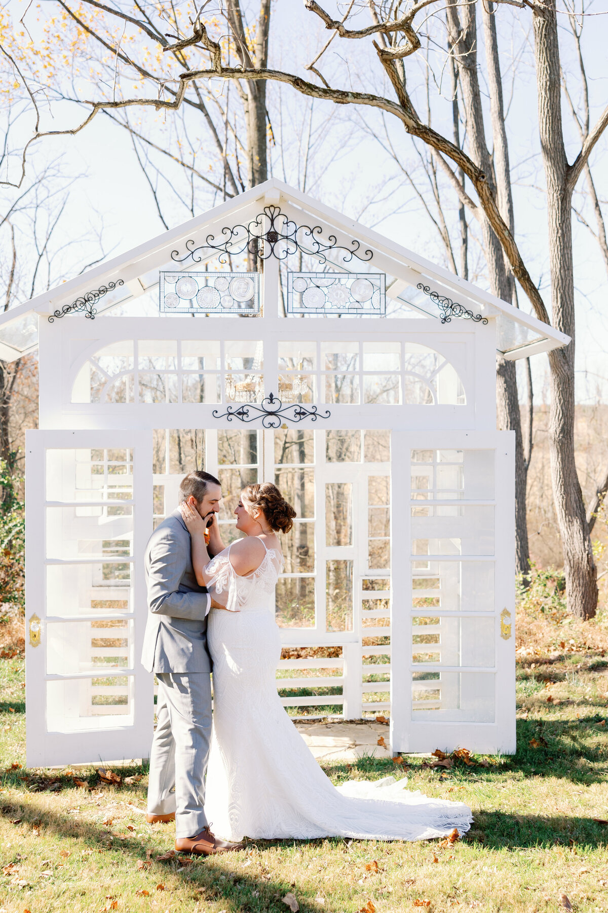 Bride and groom sharing kiss beneath white arbor surrounded by fall foliage at Carolina Home and Gardens