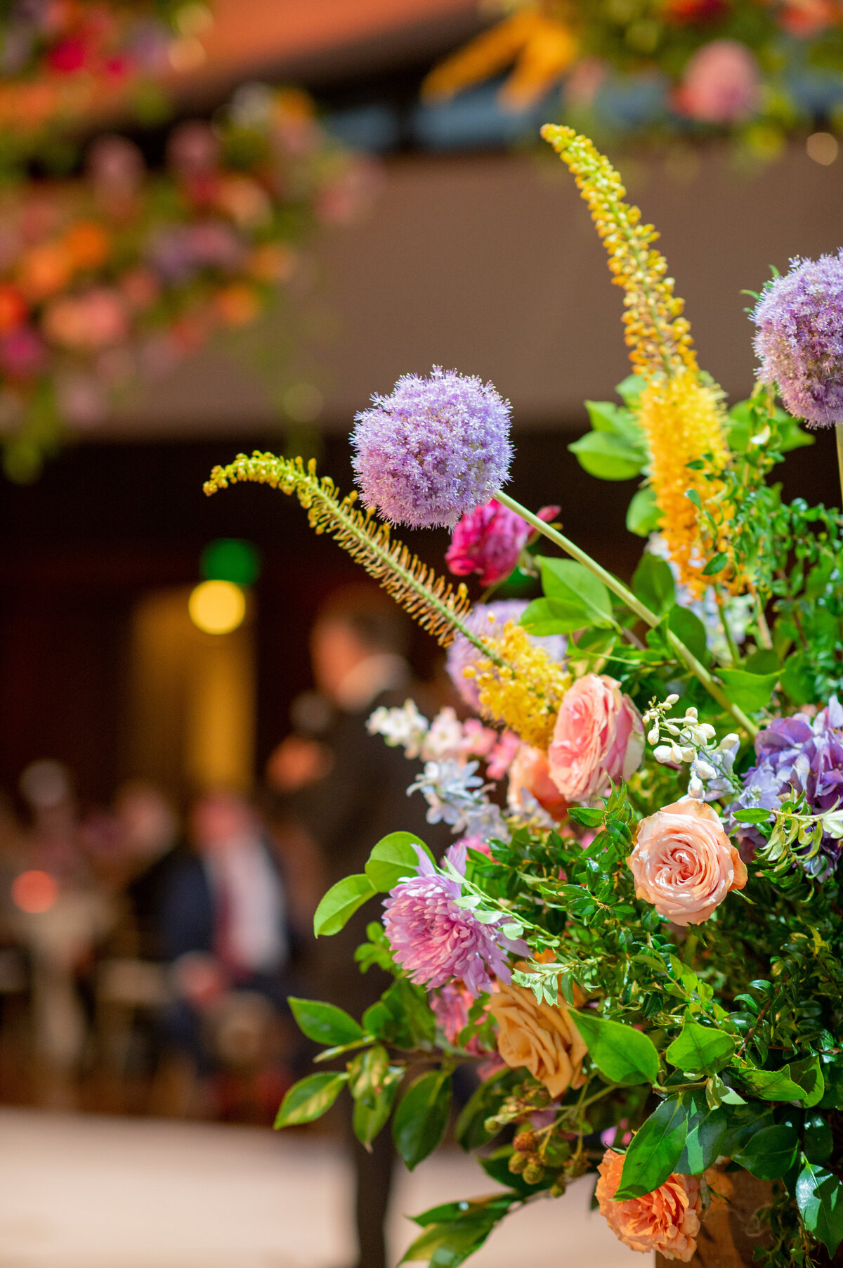 Cheerful sunset inspired summer wedding composed of petal heavy roses, garden roses, allium, orchids, ranunculus, eremurus, delphinium, and natural greenery creating hues of rosy pink, fuchsia, lavender, orange, and golden-yellow. Design by Rosemary and Finch in Nashville, TN.