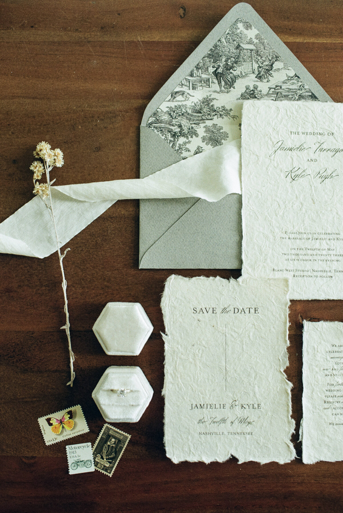 A flatlay with Save the Date's and invitations, a ring box, and some stamps. 