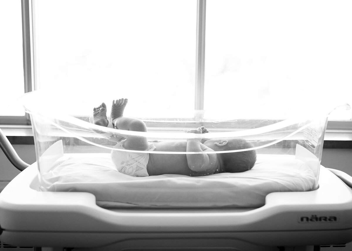 Black and white image of newborn baby in the hospital bassinet.