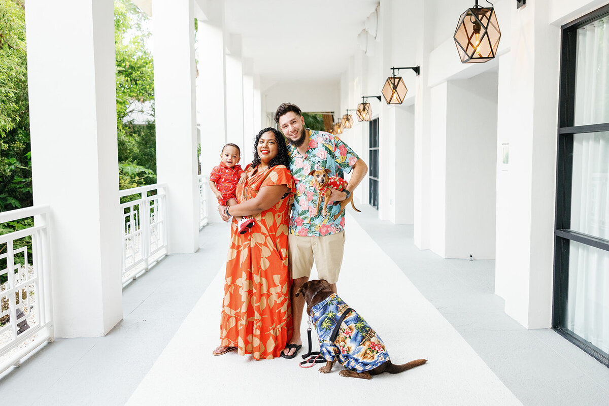 A couple holds their baby and two dogs in matching tropical outfits, capturing a joyful moment during a Florida Keys family session.